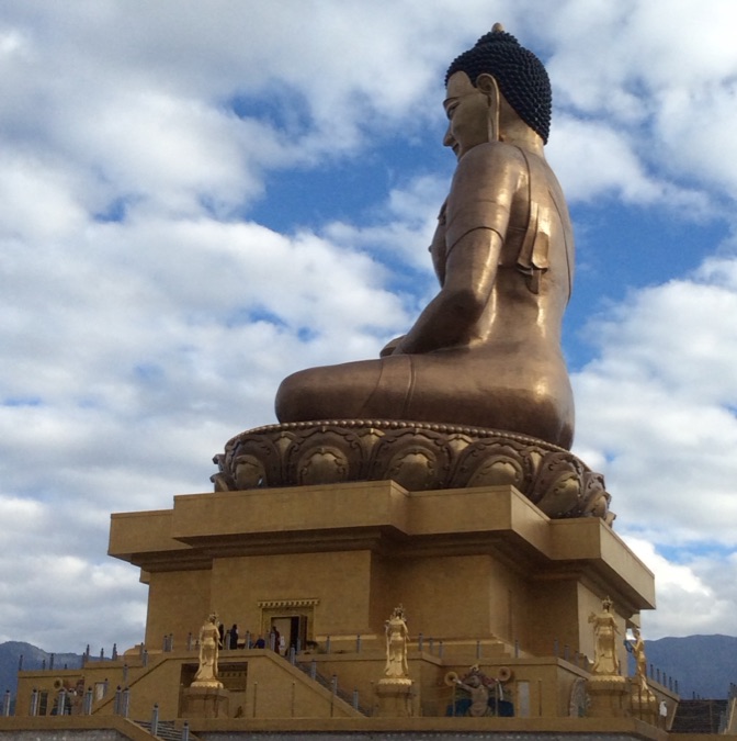 A towering seated bronze Buddha against a cloudy blue sky