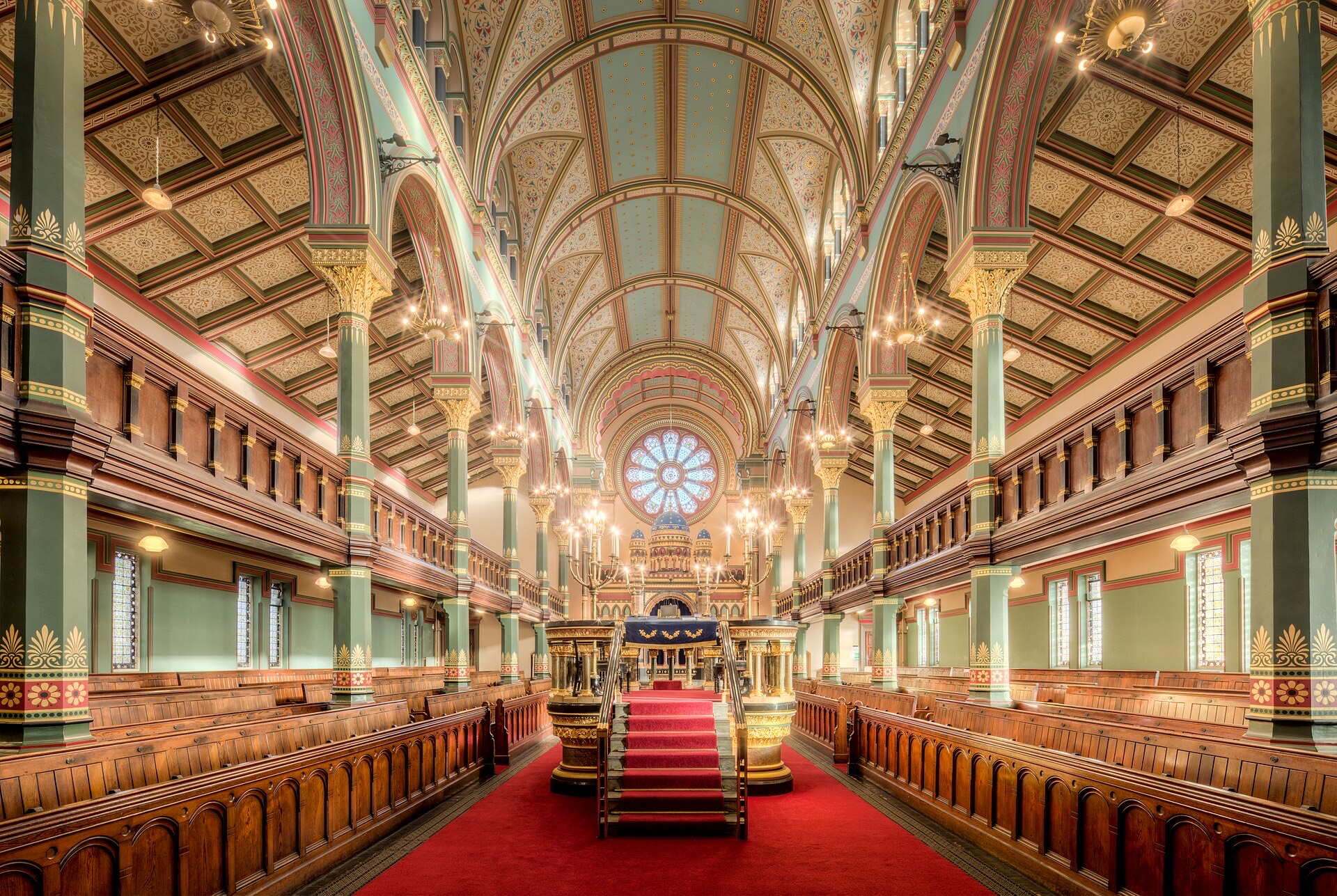 The nave of a synagogue with a red carpet and gallery seating