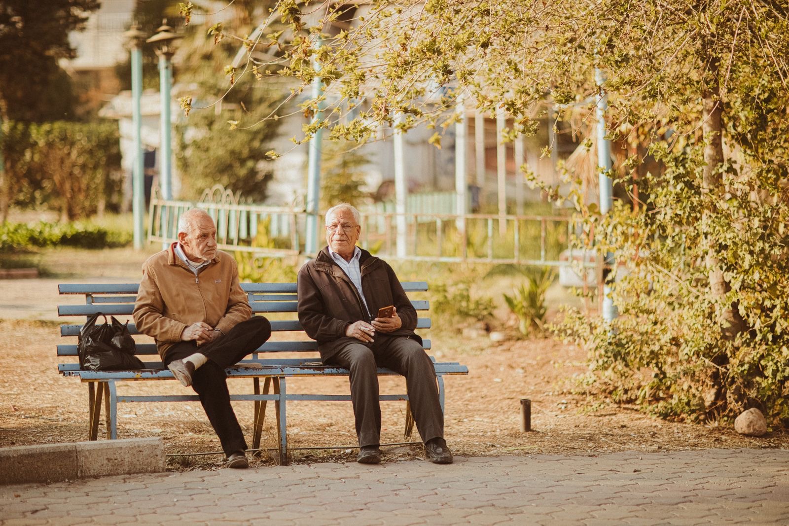 Two older friends sitting side by side on a park bench in autumn